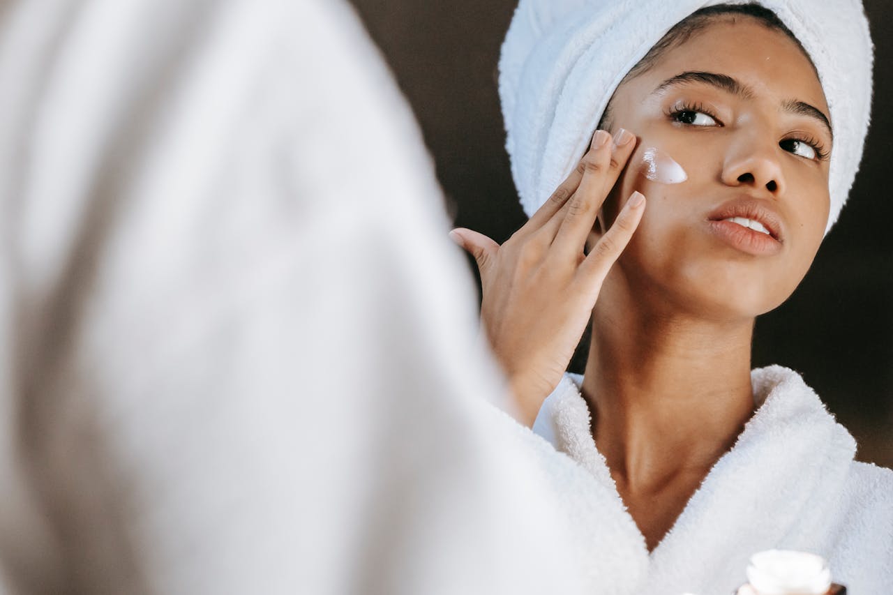 Woman in a bathrobe practices her skincare routine with moisturizing cream. Perfect for wellness themes.